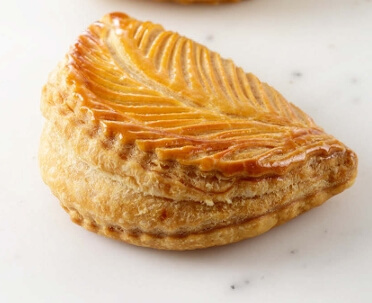 Golden apple turnovers with flaky puff pastry and glossy syrup finish, displayed on a baking tray.