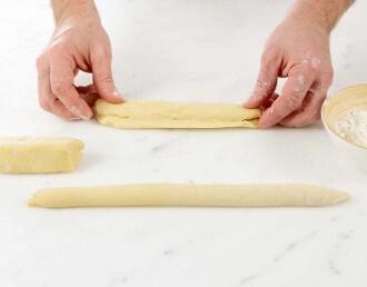 Three portions of brioche dough evenly cut on a floured work surface with a metal dough cutter beside them.