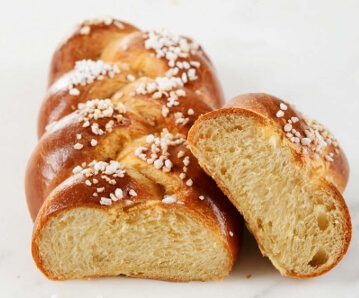 Freshly baked braided brioche resting on a cooling rack, with steam gently rising from its golden crust.