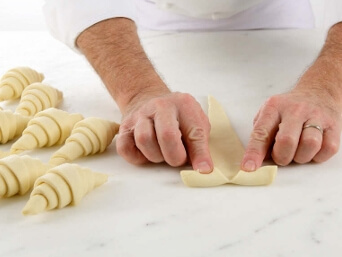 Making a small slit at the base of each croissant triangle and gently stretching the dough before rolling.