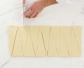 "Cutting croissant dough into evenly sized triangles, each weighing 50 to 55 grams."