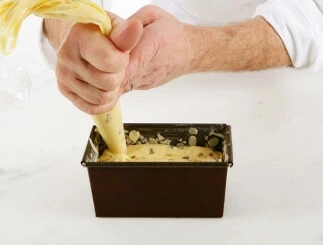A loaf pan buttered and floured, lined with sliced almonds, ready to be filled with fruitcake batter