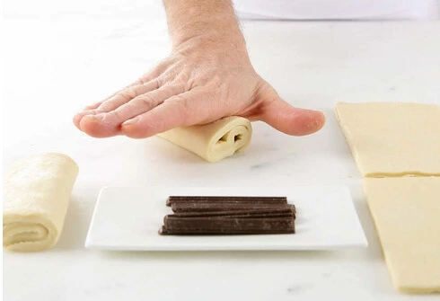 Hands gently pressing a rolled pain au chocolat to seal the seam before proofing.