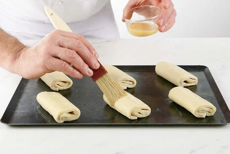 Pastry brush gently applying egg wash to proofed pain au chocolat for a golden crust.