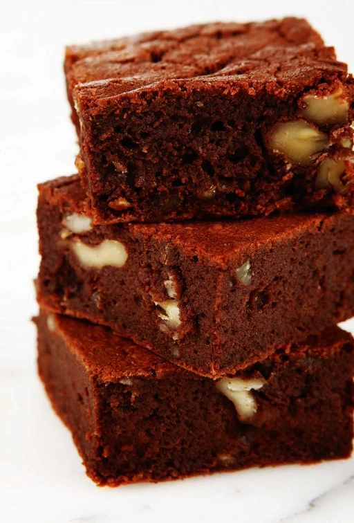 Close-up of perfectly baked brownies with a rich, fudgy texture and glossy, crackly top, served in squares.