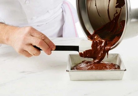 "A perfectly baked brownie with a slightly firm outer edge and a soft, fudgy center, gently pressed to check its doneness."
