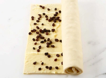 Raisins soaking in a bowl of warm water with optional rum, orange peel, and cinnamon for added flavor, ready to be used in a delicious pastry.
