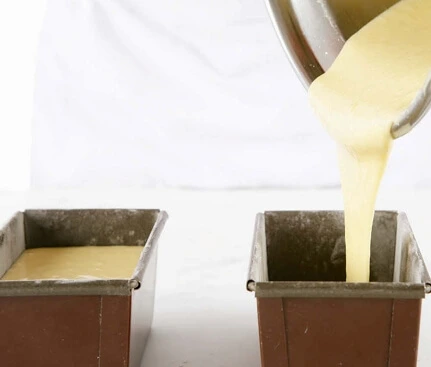 Dividing the cake batter into two loaf pans and smoothing the surface for even baking.