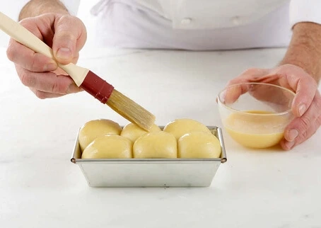 Brioche brushed with egg wash and sprinkled with pearl sugar, ready for baking.