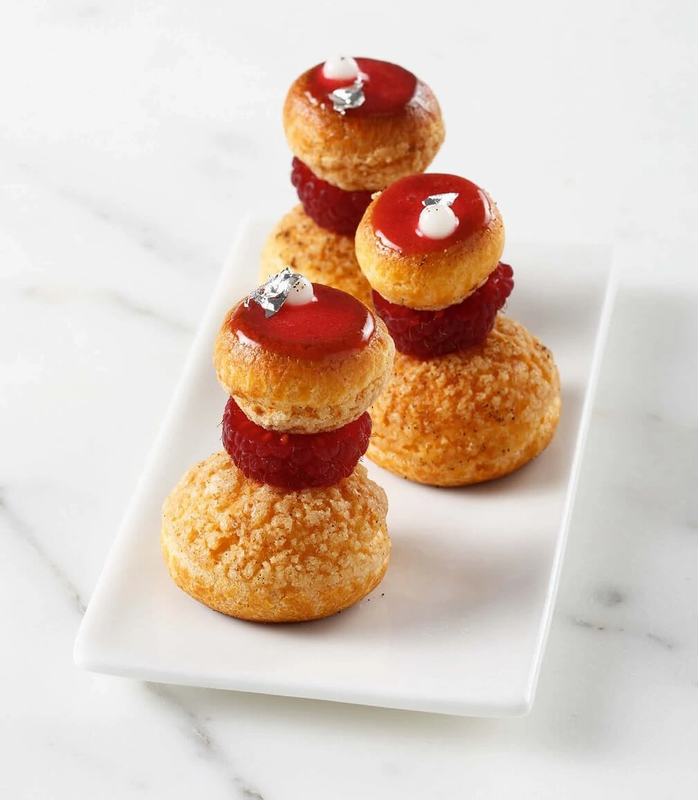 A delicate and sophisticated Vanilla-Raspberry Religieuse, with layers of rich vanilla and tangy raspberry crémeux, topped with a glossy red glaze and garnished with vanilla caviar spheres.