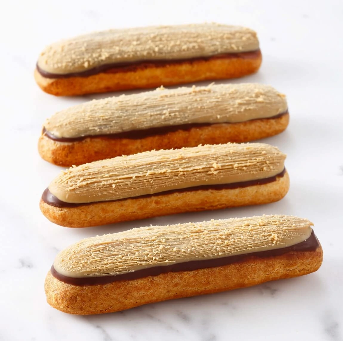 A gourmet éclair filled with coffee mascarpone cream, topped with dark chocolate and Dulcey glaze, finished with a brushed decorative texture.