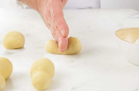A baker shaping the dough for Petites Brioches à Tête, creating a smooth log and forming the iconic "head" with precision.