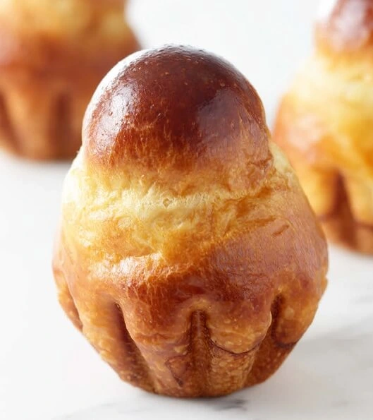 A freshly baked Petites Brioche à Tête being carefully removed from its mold to maintain its shape and texture.