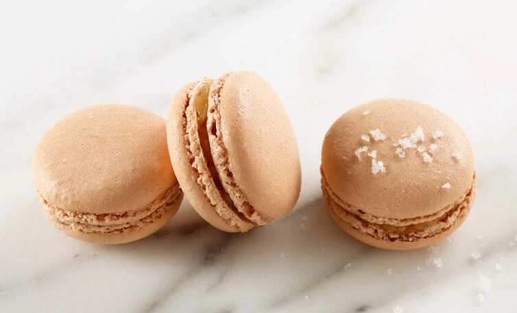 Close-up of golden brown salted butter caramel macarons with smooth caramel filling, showcasing delicate, glossy shells and a tender interior.