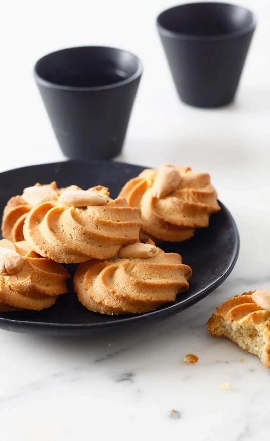 Piped shortbread cookies shaped into rosettes with almonds on top, displayed on a silicone baking mat.