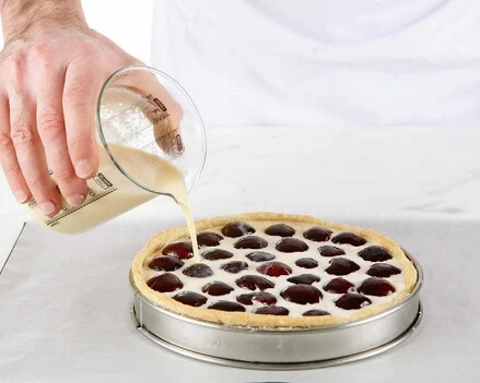 Photo of a freshly assembled tart with a smooth filling inside a golden crust, ready to be baked in the oven