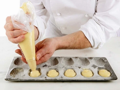 A piping bag fitted with a plain 10mm tip, ready to perfectly fill Madeleine molds.