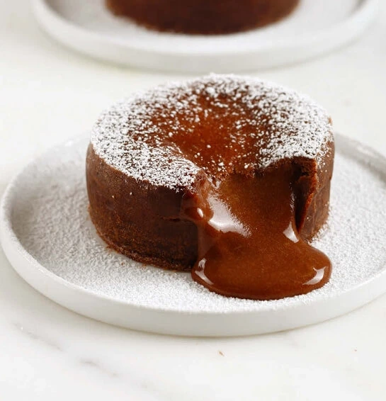 A plated moelleux au chocolat just out of the oven, with a molten chocolate center gently oozing out, garnished with ice cream and fresh berries.