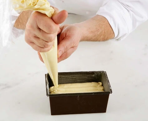 Batter being transferred into a piping bag, ready to be poured into a greased and floured loaf pan
