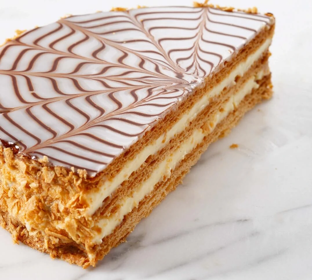 "Homemade millefeuille with layers of golden puff pastry, vanilla pastry cream, and glossy fondant icing with chocolate decoration
