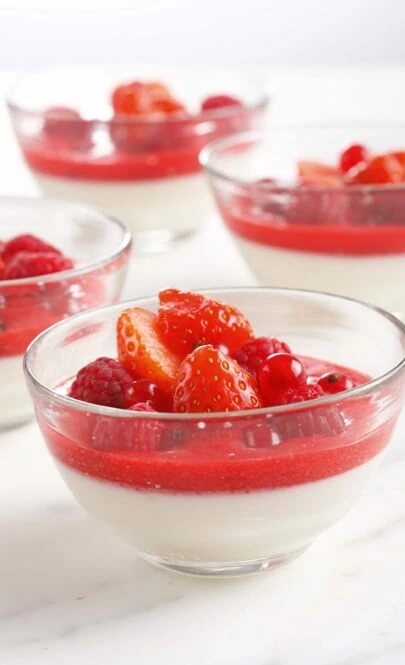 Creamy homemade lime yogurt topped with fresh berries and fruit coulis in a clear glass
