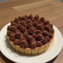 Overhead view of a glossy milk chocolate tart set in a cocoa pastry crust, resting on a marble surface