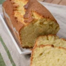 Slice of golden vanilla sponge cake with soft, airy crumb on a white plate, decorated with light dusting of powdered sugar.