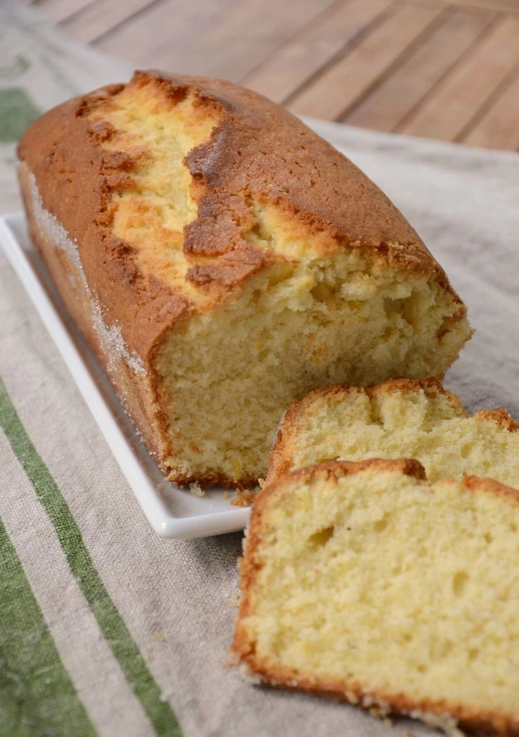 Slice of golden vanilla sponge cake with soft, airy crumb on a white plate, decorated with light dusting of powdered sugar.